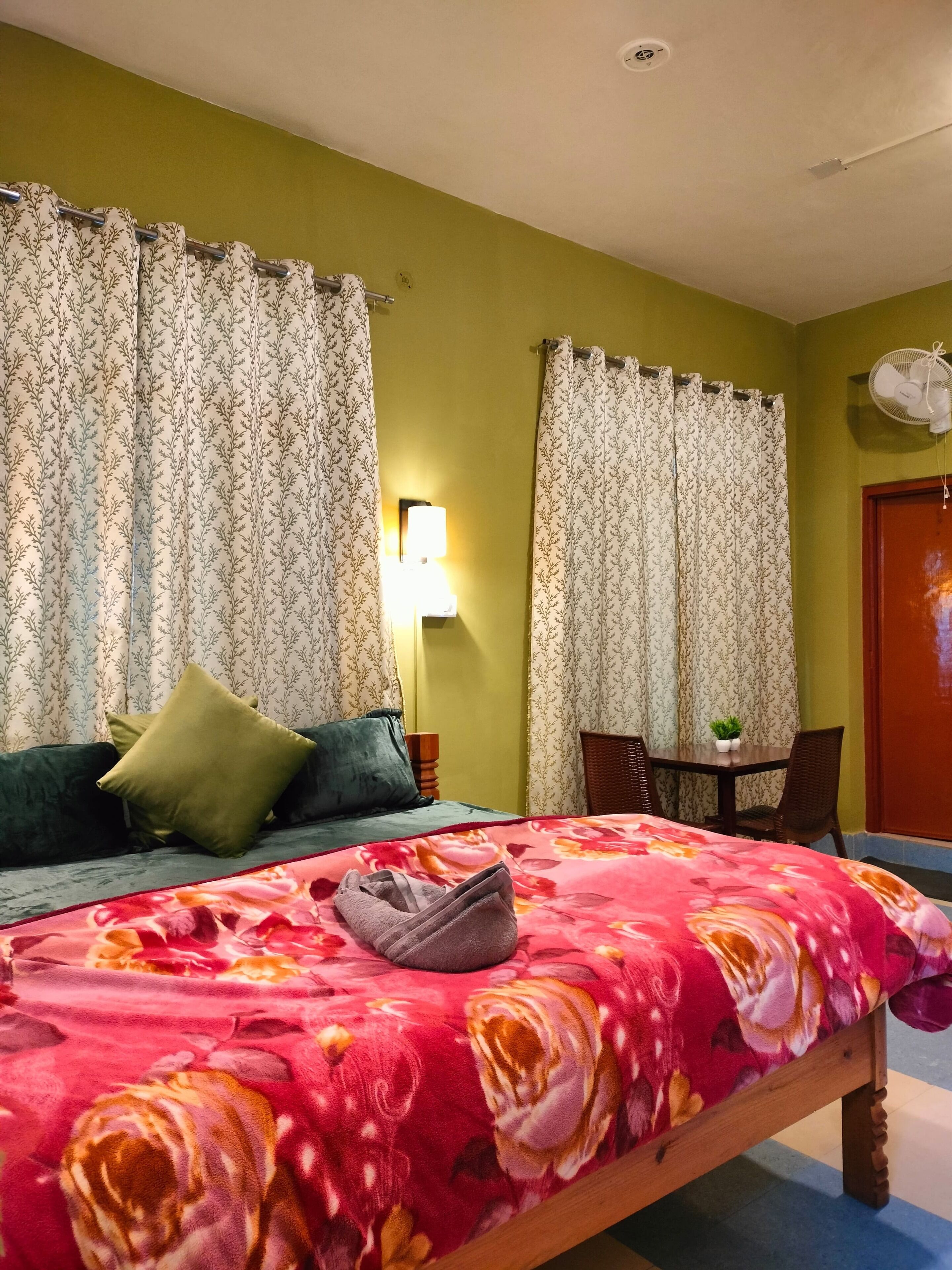 Una habitación con cama, una mesa y sillas, una lámpara y cortinas.