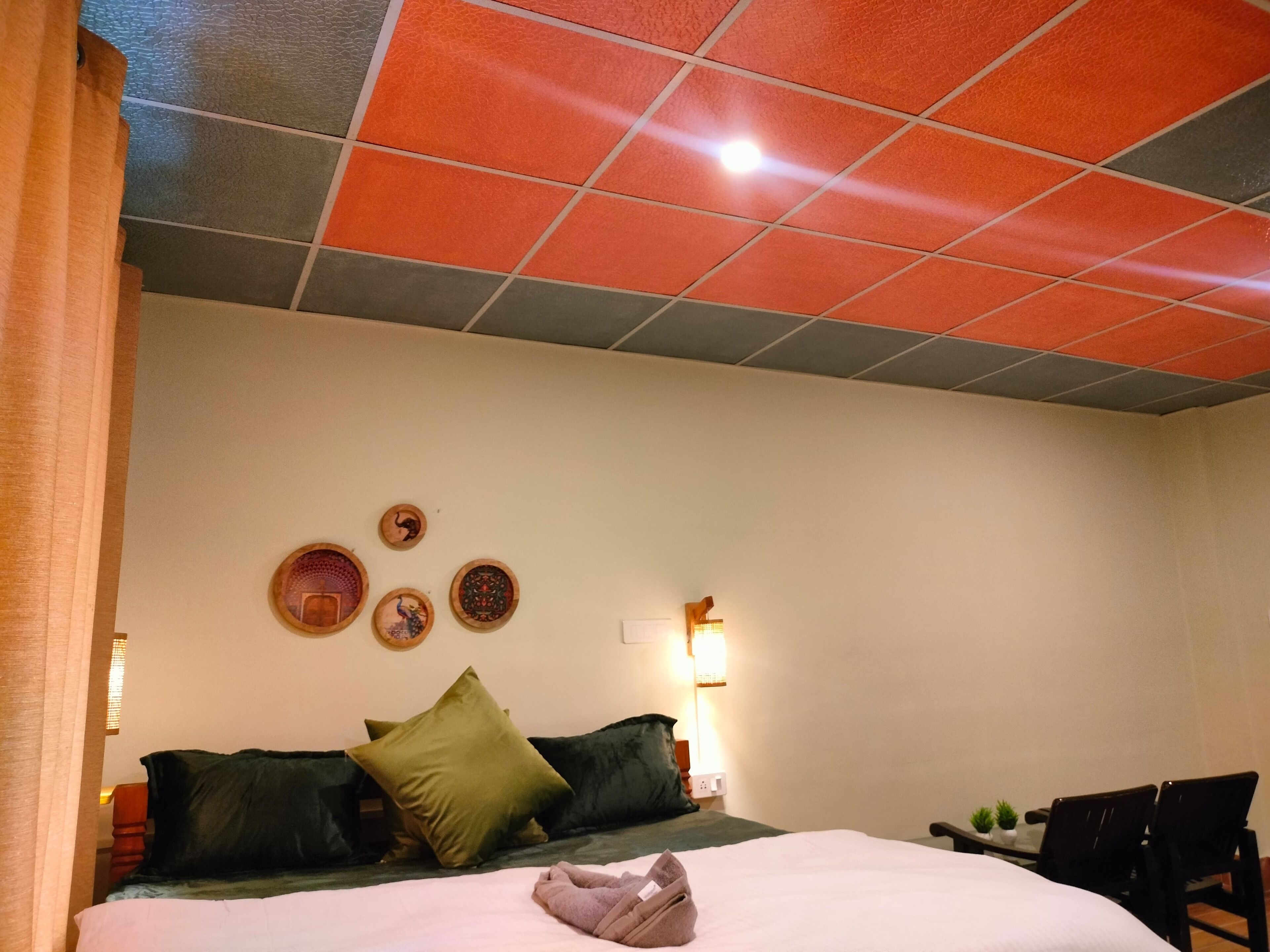 Una habitación de hotel con cama, almohadas, mesita de noche, lámpara y decoración en la pared.