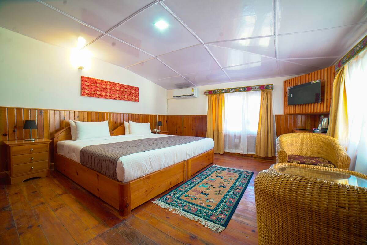 A bedroom with a wooden bed, a nightstand, a wicker chair, a TV mounted on the wall, and a patterned rug.