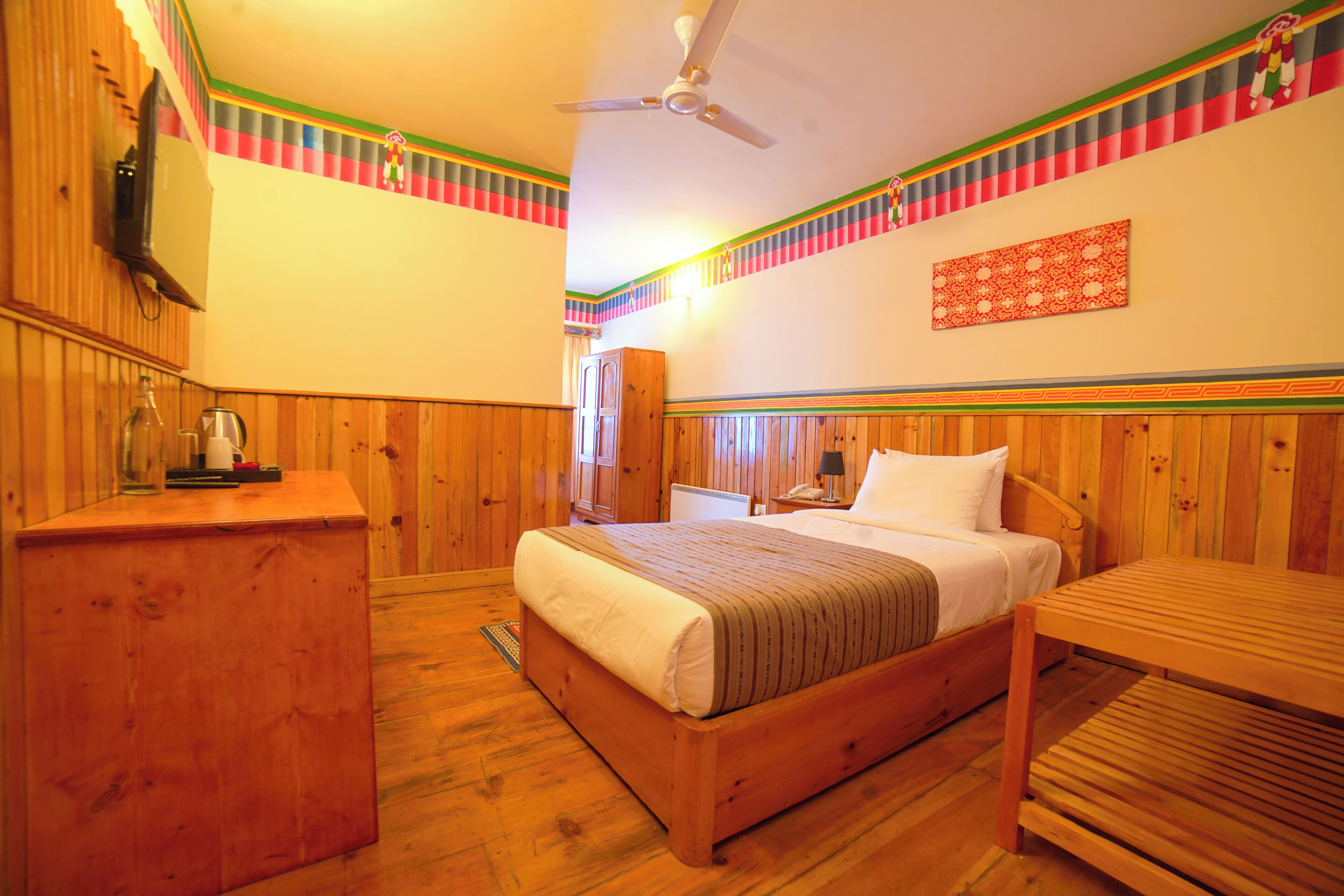 A wooden-paneled room with a bed, a desk, and a ceiling fan.