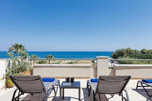 A terrace with two lounge chairs and a table, overlooking a beach and the sea.
