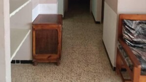 Ein schmaler Flur mit einem Holzschrank, einer Uhr und einem an der Wand befestigten Fernseher.