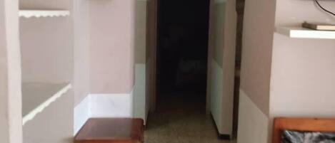 A narrow hallway with a wooden cabinet, a clock, and a television mounted on the wall.