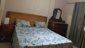 Ein Schlafzimmer mit einem hölzernen Bett, einem Nachttisch mit Lampe, einer Kommode und einem Spiegel.