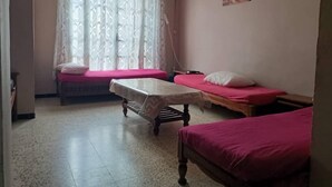 Ein Zimmer mit zwei Betten, einem kleinen Tisch und einem Fenster mit Vorhängen.