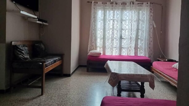 Ein Zimmer mit Bett, Tisch, Stuhl, einem an der Wand befestigten Fernseher und einem Fenster mit Vorhängen.