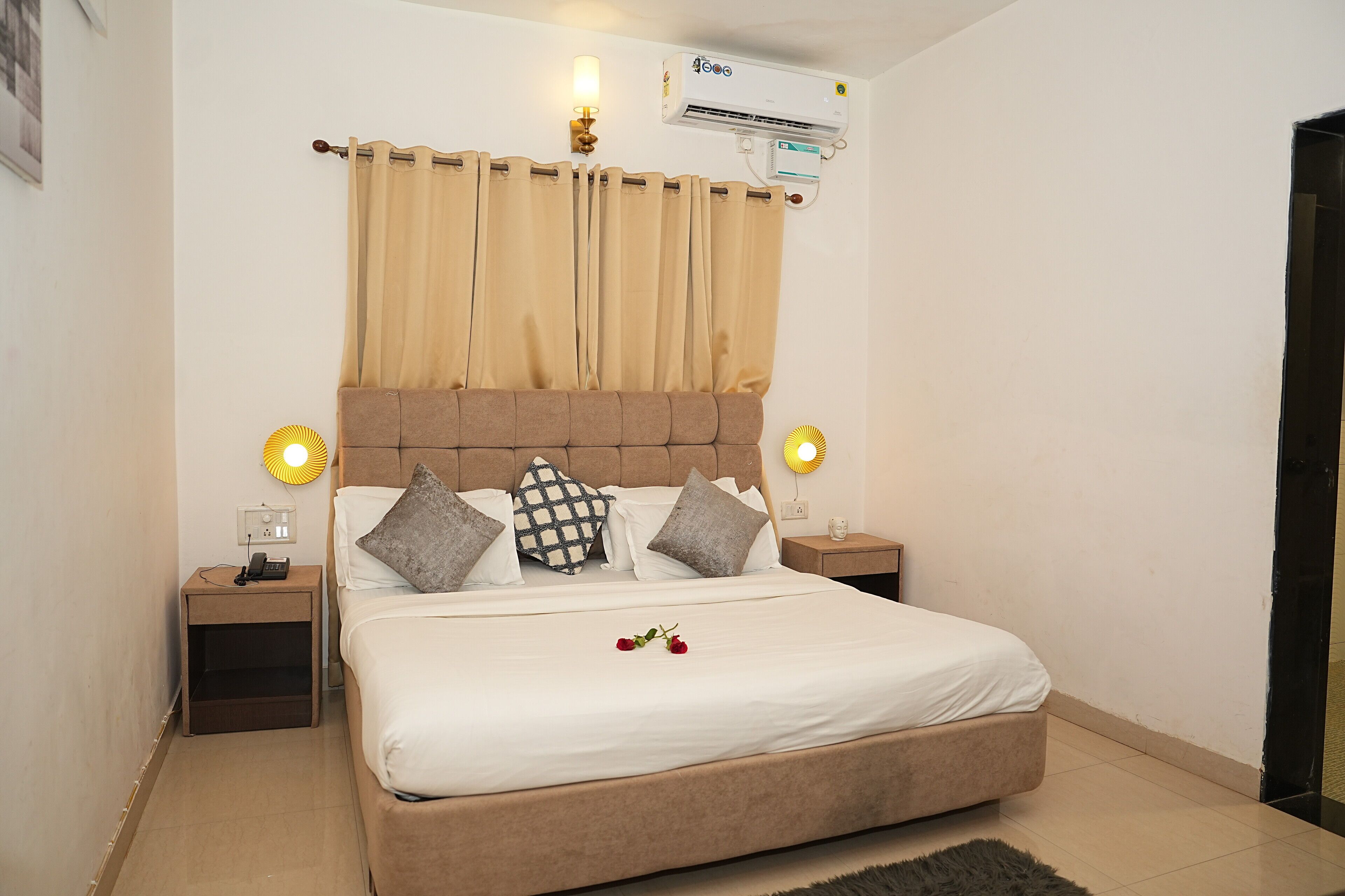 A bedroom with a bed, curtains, bedside lamps, a nightstand, and an air conditioning unit.