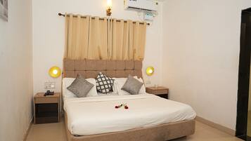 A bedroom with a bed, curtains, bedside lamps, a nightstand, and an air conditioning unit.