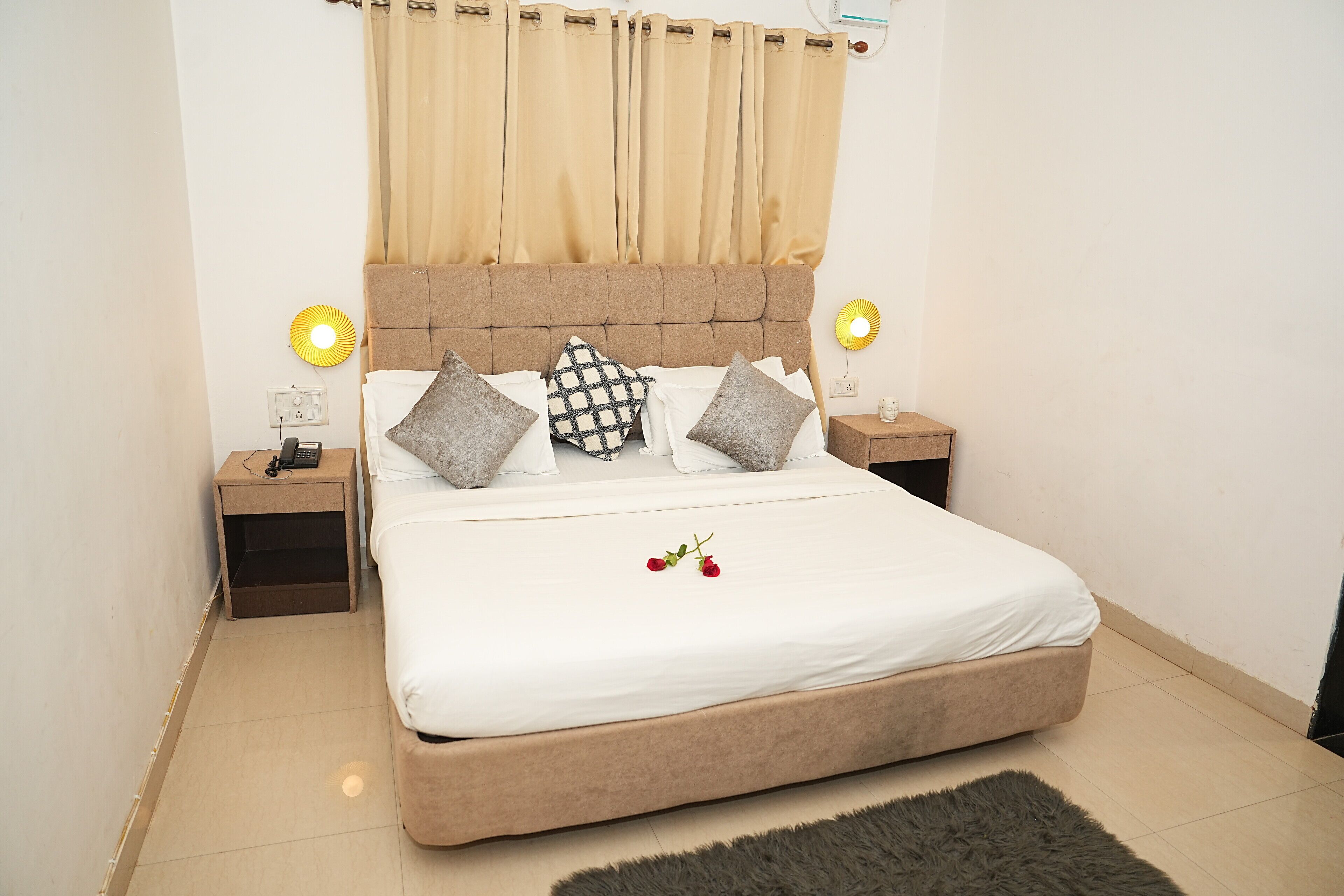 A neatly made bed with white bedding, two bedside tables with lamps, and a large window with beige curtains.