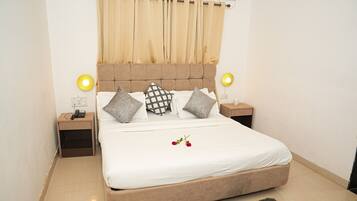 A neatly made bed with white bedding, two bedside tables with lamps, and a large window with beige curtains.