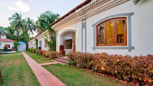 Un edificio blanco con techo de tejas rojas, un camino que lleva a la entrada y un jardín bien cuidado con palmeras y arbustos.