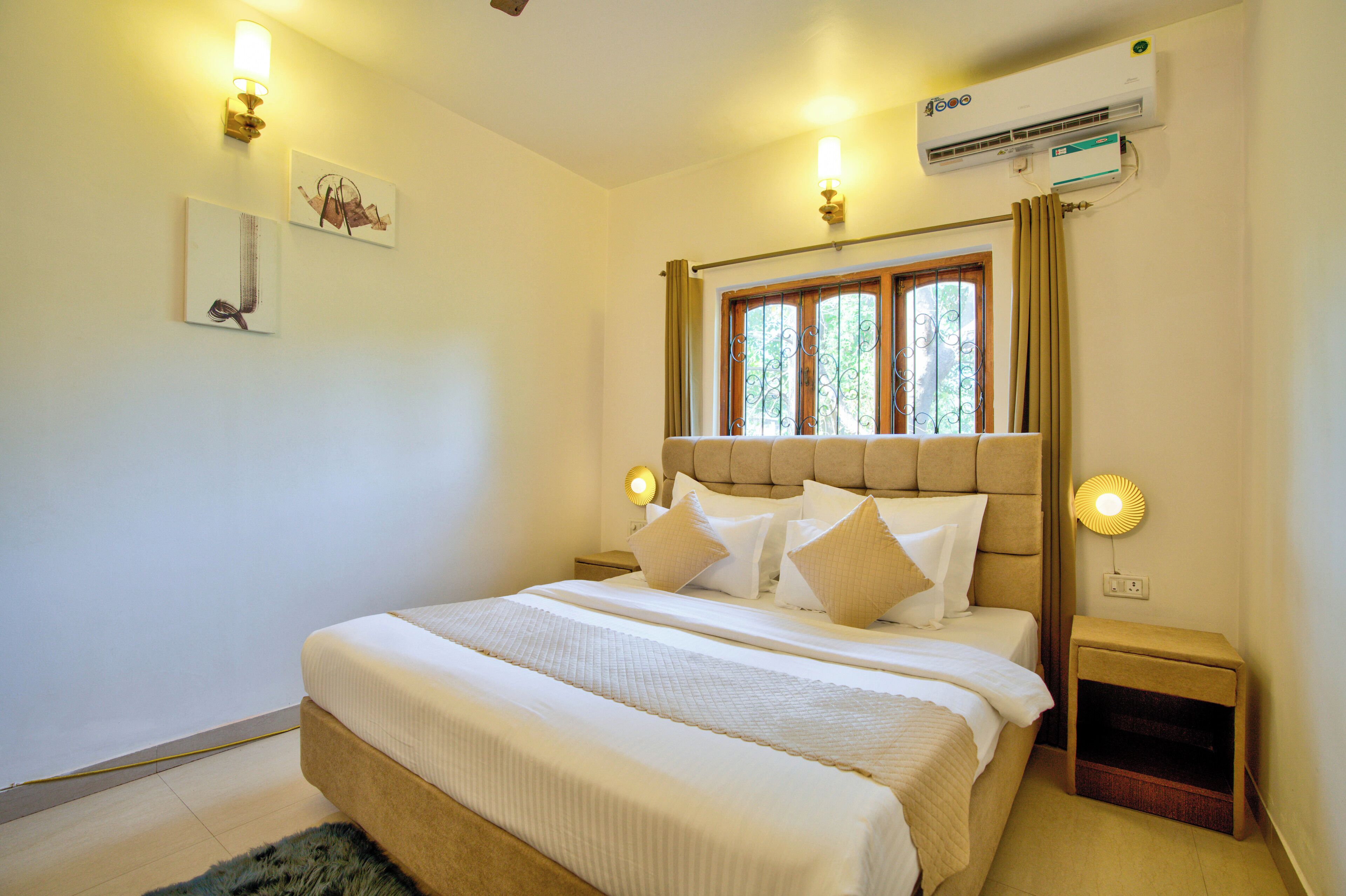 A neatly made bed with a headboard, bedside lamps, and a window with curtains.
