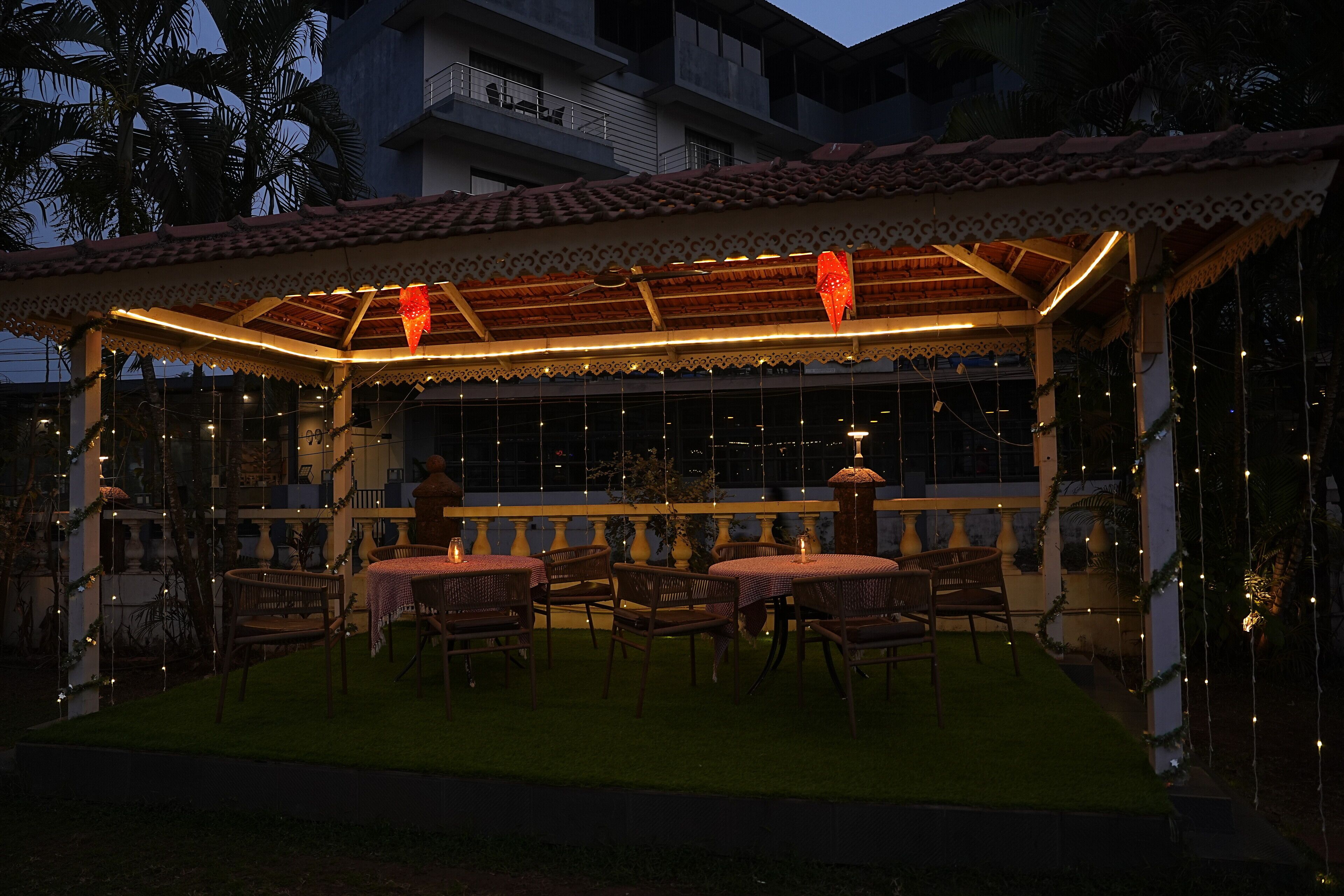 An outdoor patio with tables and chairs, a covered area with a tiled roof, and string lights.