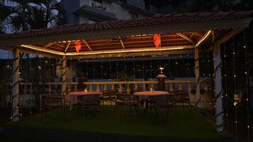 An outdoor patio with tables and chairs, a covered area with a tiled roof, and string lights.