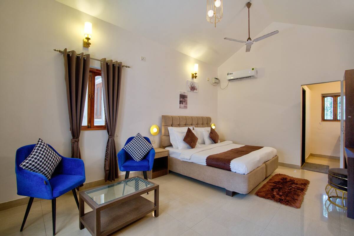 Une chambre d’hôtel comprenant un lit, deux chaises, une table basse en verre, un ventilateur de plafond et un appareil de climatisation.