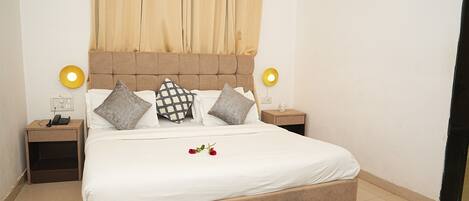 A neatly made bed with a white duvet, two bedside tables with lamps, and a curtain.