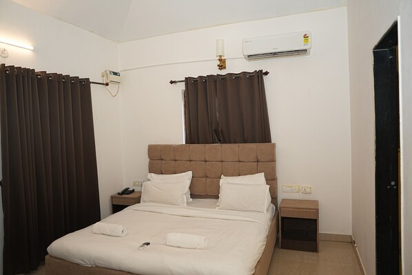 A hotel room with a large bed, two bedside tables, a nightstand, a telephone, and an air conditioning unit.