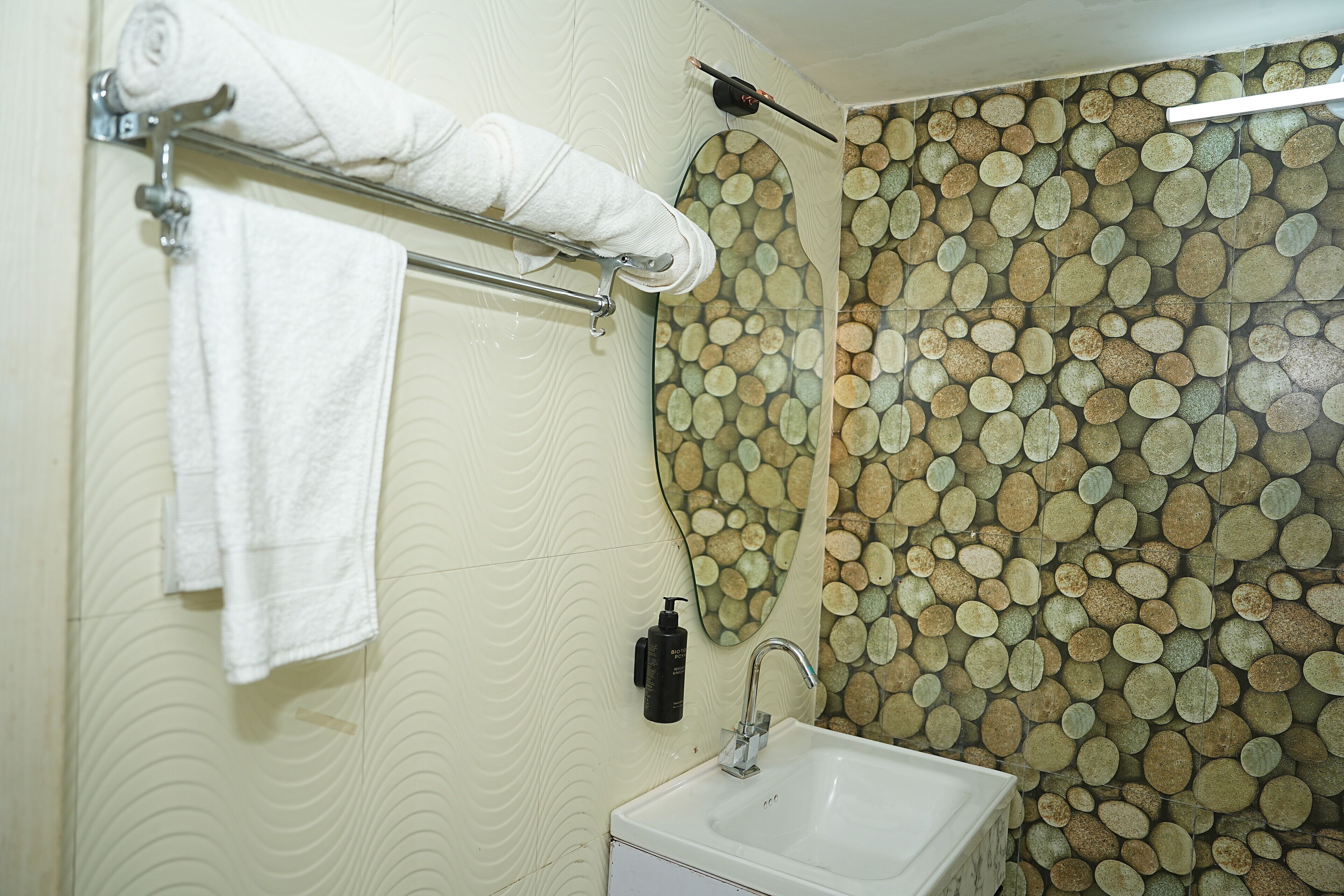 Ein Badezimmer mit Waschbecken, Handtuchhalter mit gerolltem Handtuch, Seifenspender und dekorativer Wand mit kreisförmigen Mustern.