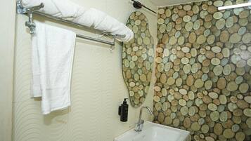 Ein Badezimmer mit Waschbecken, Handtuchhalter mit gerolltem Handtuch, Seifenspender und dekorativer Wand mit kreisförmigen Mustern.