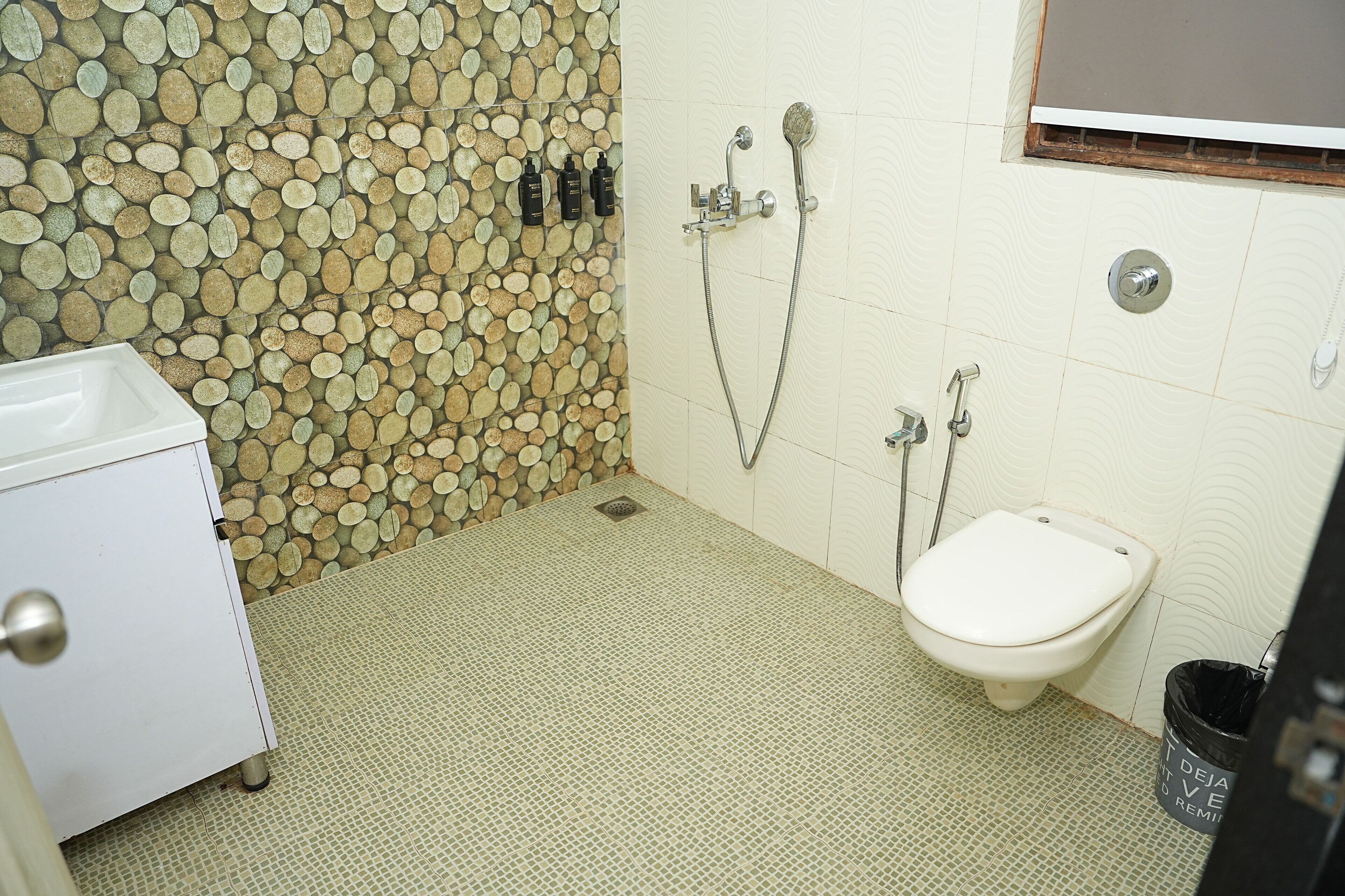 A bathroom with a mosaic wall, a toilet, a sink, and a trash bin.