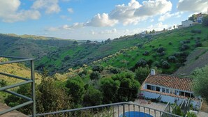 A hillside view with a white building with a tiled roof and a blue pool in the foreground.