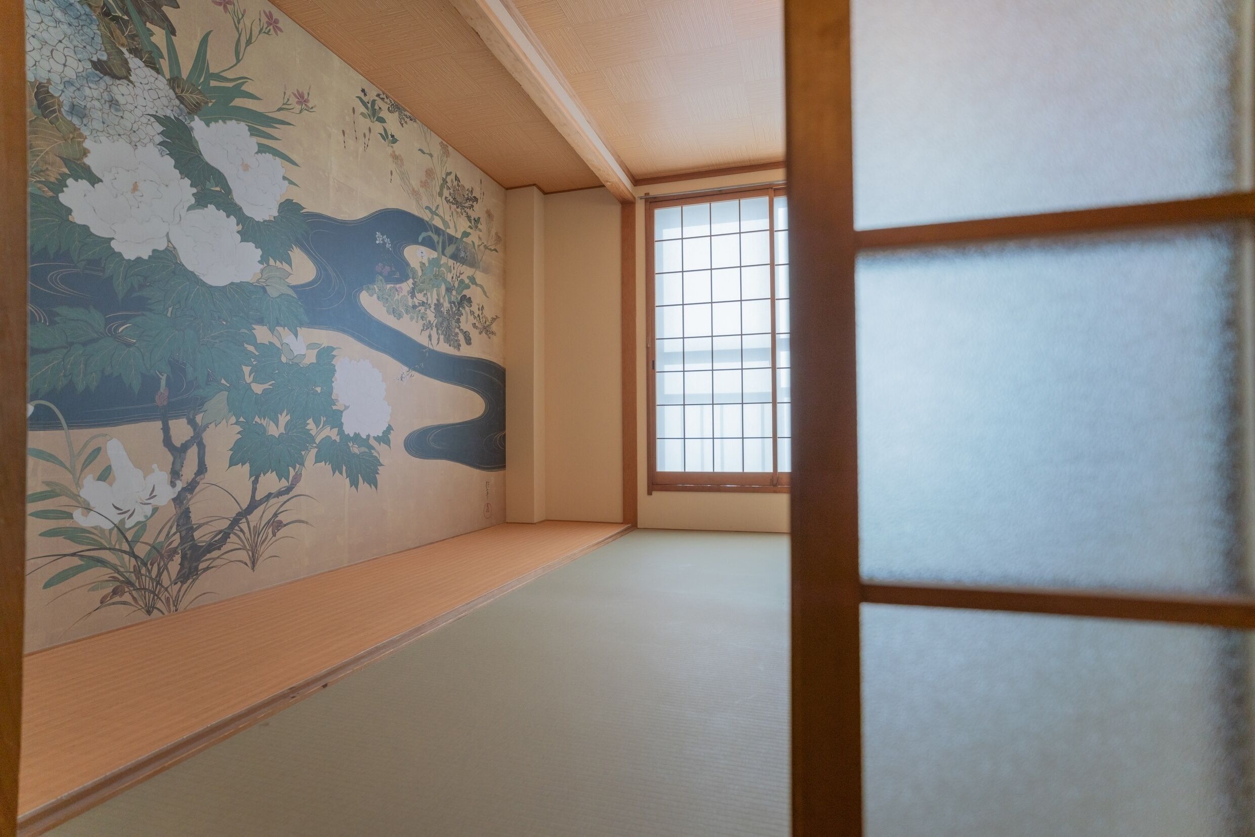 A traditional Japanese room with tatami flooring, a shoji screen, and a mural of nature.