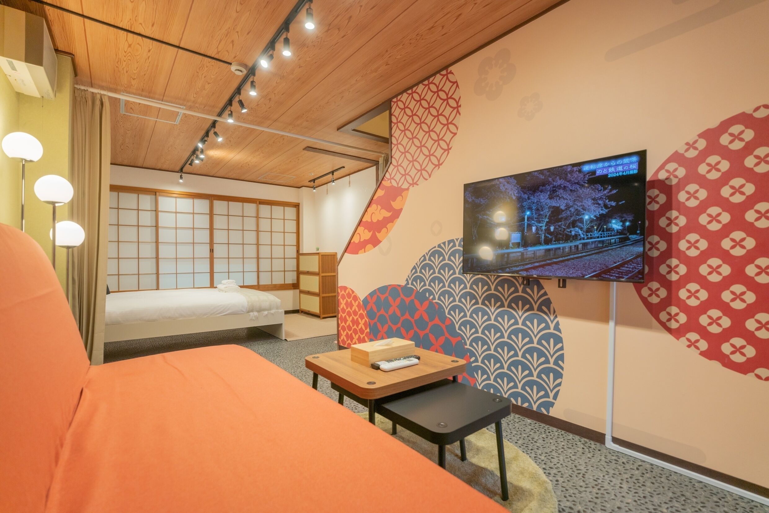 A hotel room with a bed, a TV mounted on the wall, a small table, and a traditional Japanese sliding door.