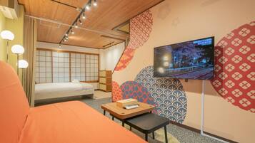 A hotel room with a bed, a TV mounted on the wall, a small table, and a traditional Japanese sliding door.
