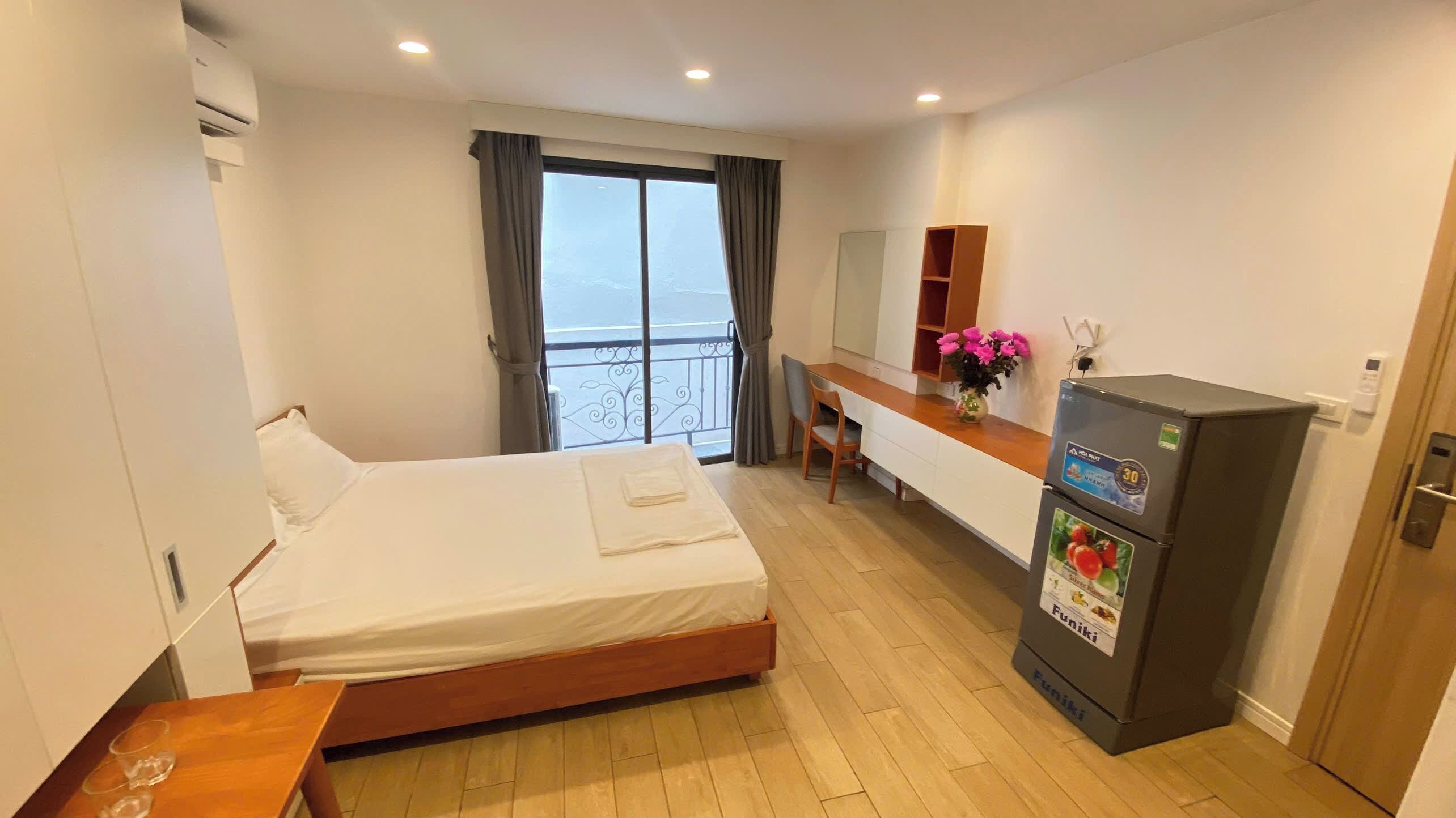A hotel room with a bed, a desk, a refrigerator, and a view of the outside.