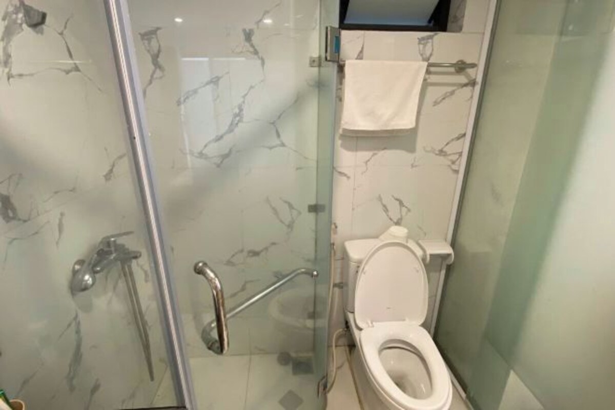 Un baño con ducha envuelta en vidrio, inodoro blanco y pared con diseño de mármol.