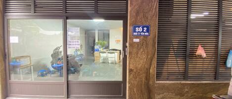 Ein Gebäude mit einer großen Glasdoor und einem Schild, das Zimmer Nummer 2 anzeigt. Innen befinden sich Tische und Stühle, was auf einen Ess- oder Besprechungsbereich hindeutet.