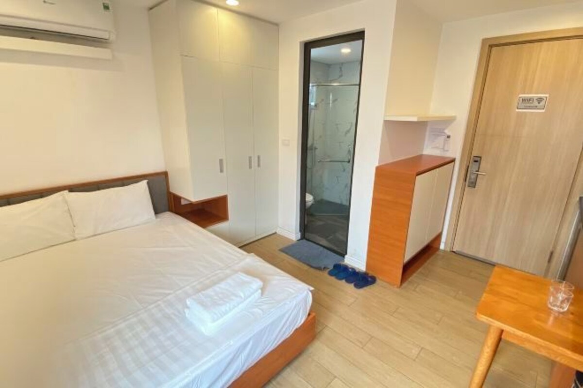 Habitación de hotel con cama, escritorio de madera, zona de ducha y armario.