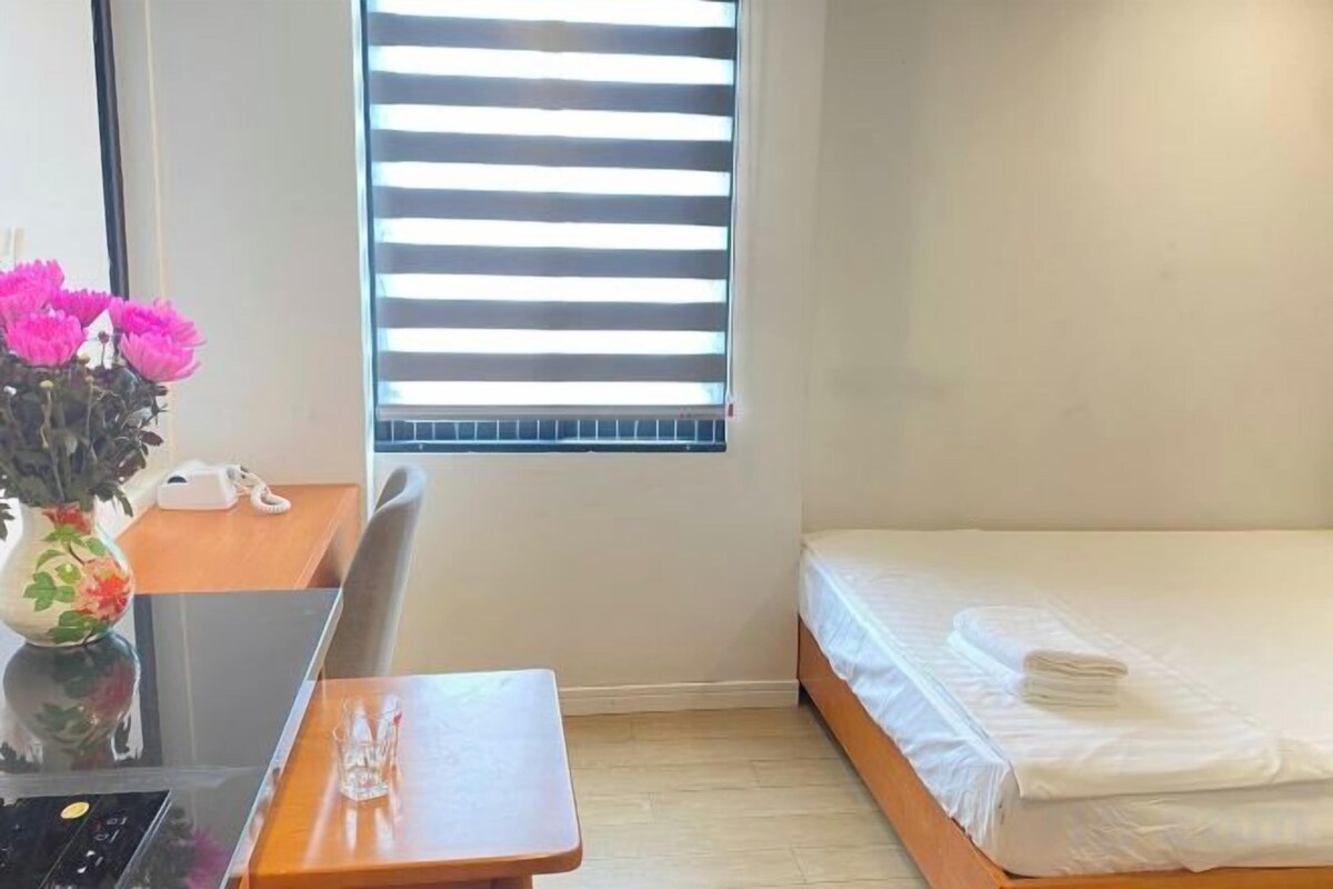 A small room with a bed, a desk with a computer, and a window with blinds.