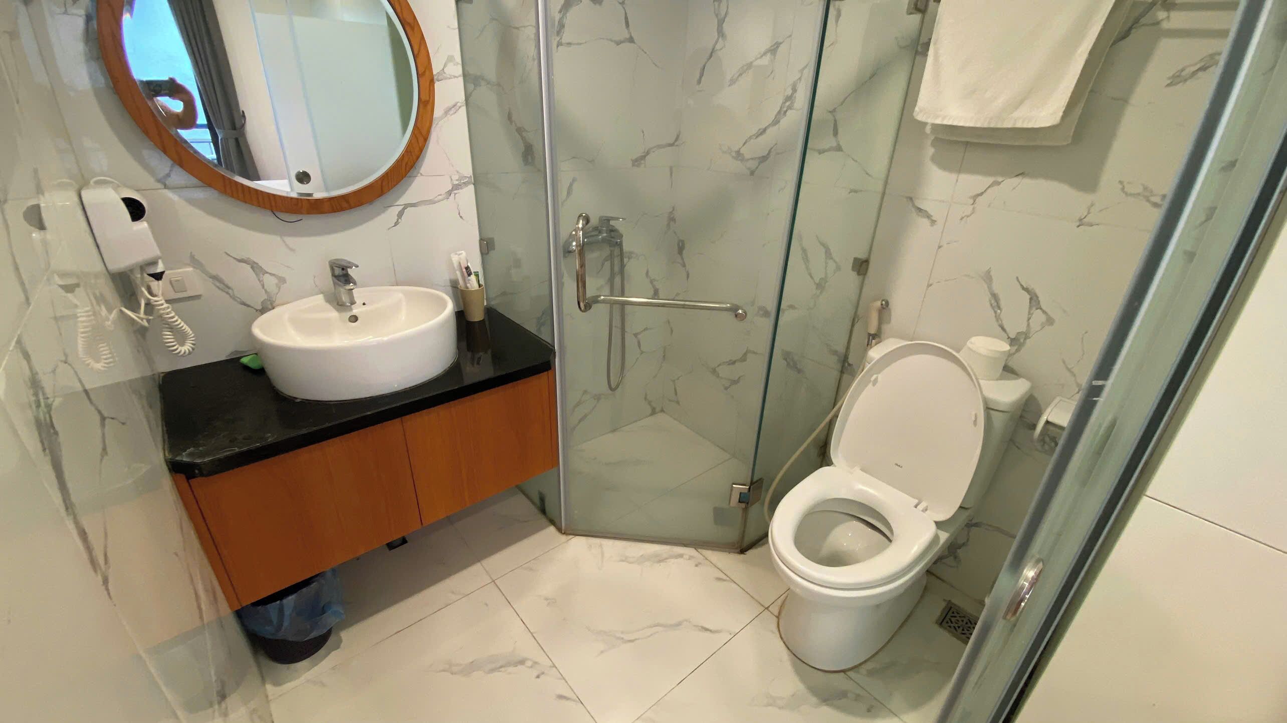Un baño con lavamanos blanco, espejo, cabina de ducha con mampara de vidrio y retrete.