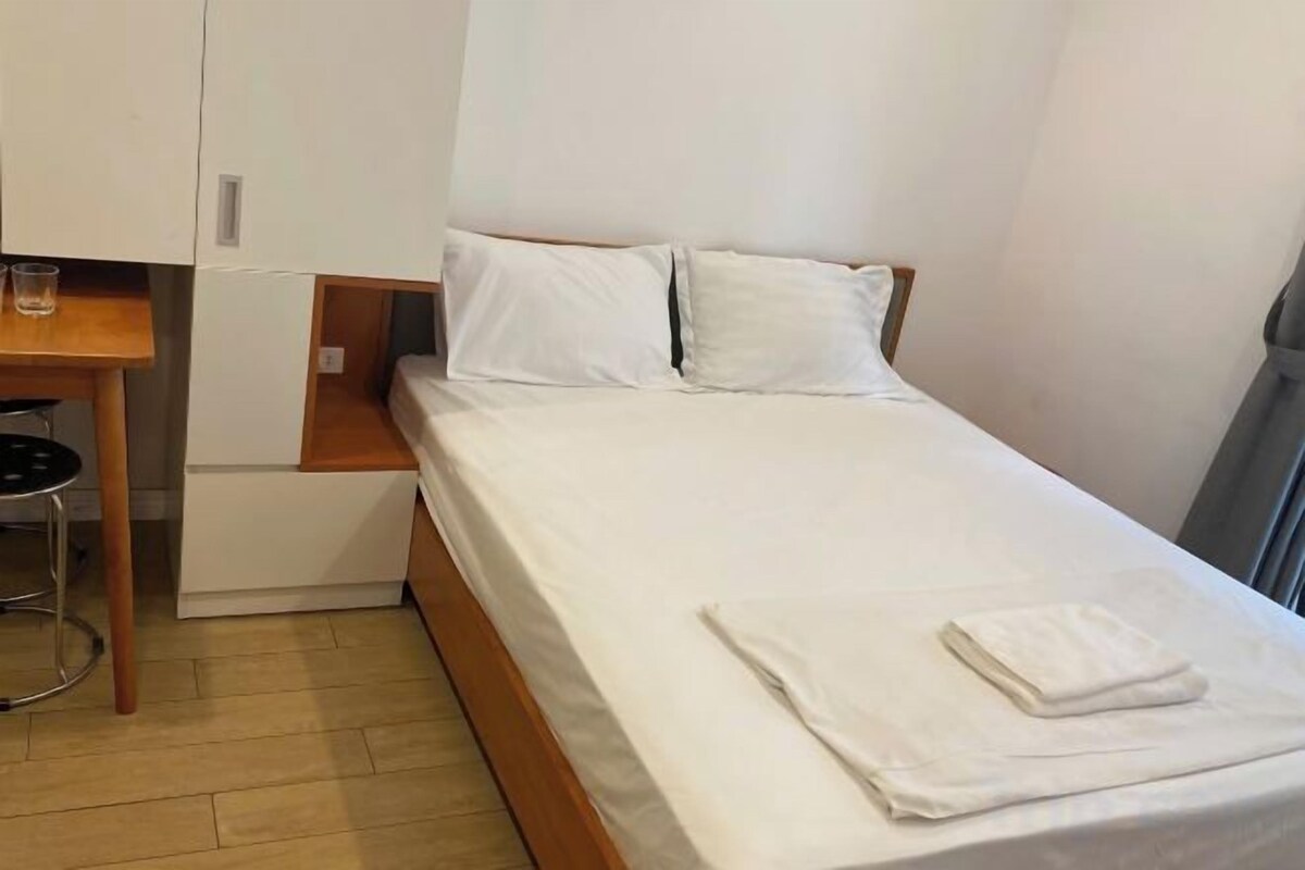 A single bed with white linens, a wooden nightstand, and a small table with a chair.