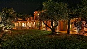 A well-lit, two-story house with a spacious patio, surrounded by trees and a well-maintained lawn.