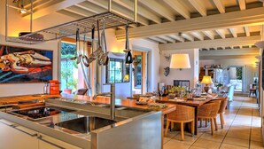 A modern kitchen with stainless steel appliances, a dining area with wicker chairs, and a large painting on the wall.