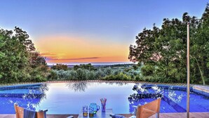 A swimming pool with lounge chairs and a view of the sunset.