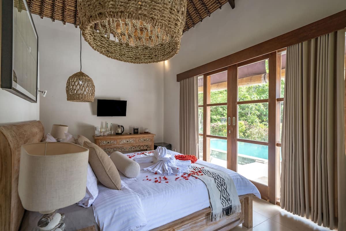 A well-appointed bedroom with a large bed, a television, a dresser, and a view of a swimming pool.
