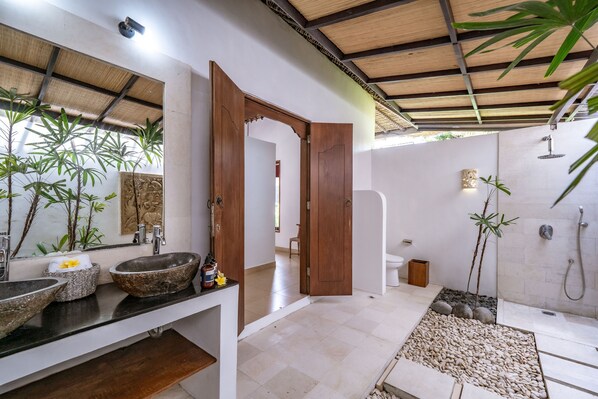 A modern bathroom with a large mirror, two stone sinks, a wooden door, a shower area, and a small indoor garden. - JENDI Village (Ungasan)