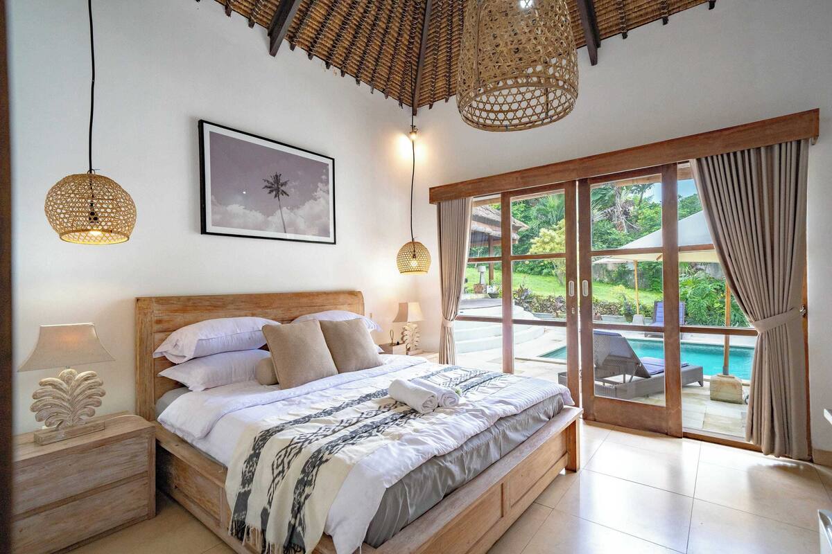 A bedroom with a large bed, wooden headboard, and a view of a pool through a sliding glass door.