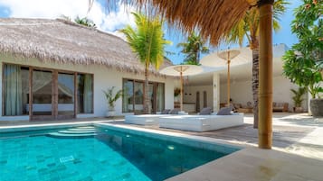 Un resort con piscina, edifici a tetto di paglia e zone relax all'aperto.