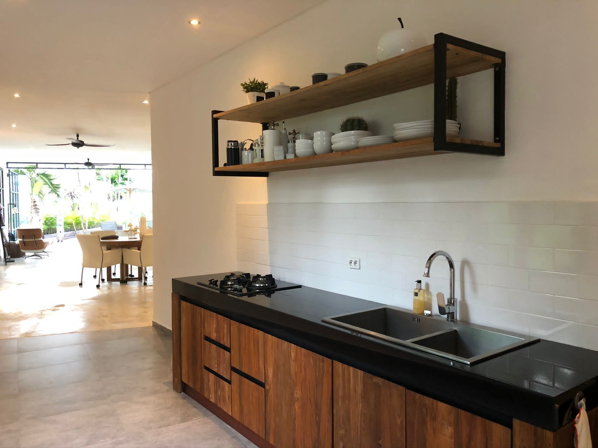 A modern kitchen with a black countertop, wooden cabinets, and a built-in sink. There is a shelf above the sink with decorative items and a mirror.
