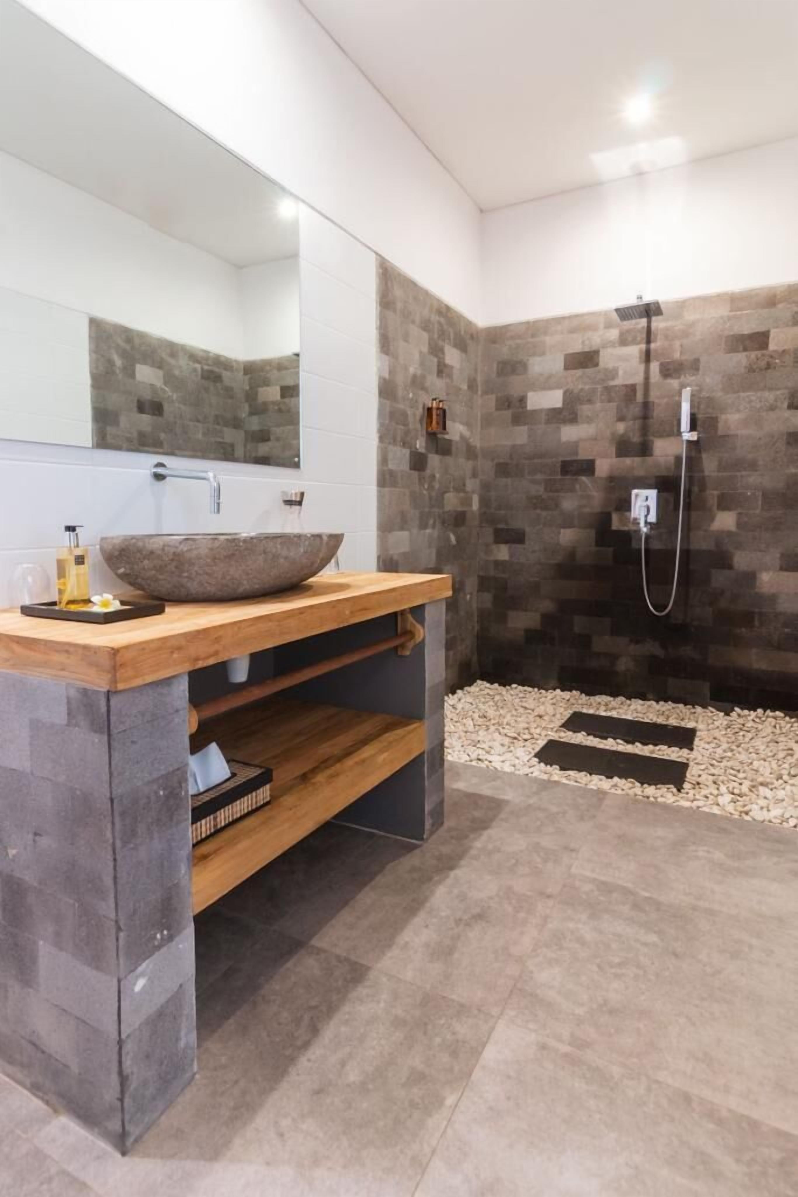 Un baño moderno con lavamanos de piedra, un espejo grande y una zona de ducha con pared de azulejos.