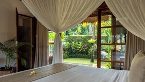 A bedroom with a large bed, a view of a lush garden, and a thatched roof structure. - Lempuyang Boutique Hotel (Karangasem)