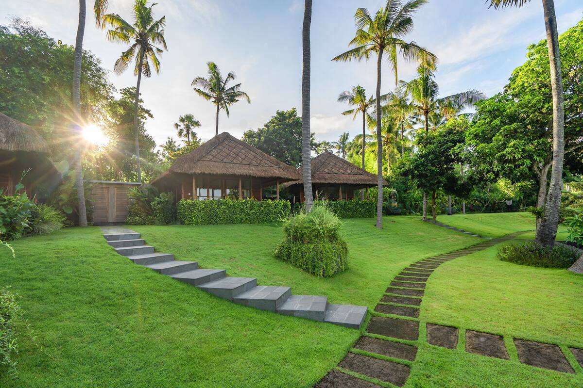 A tropical resort with thatched-roof huts, a well-manicured lawn, and palm trees.