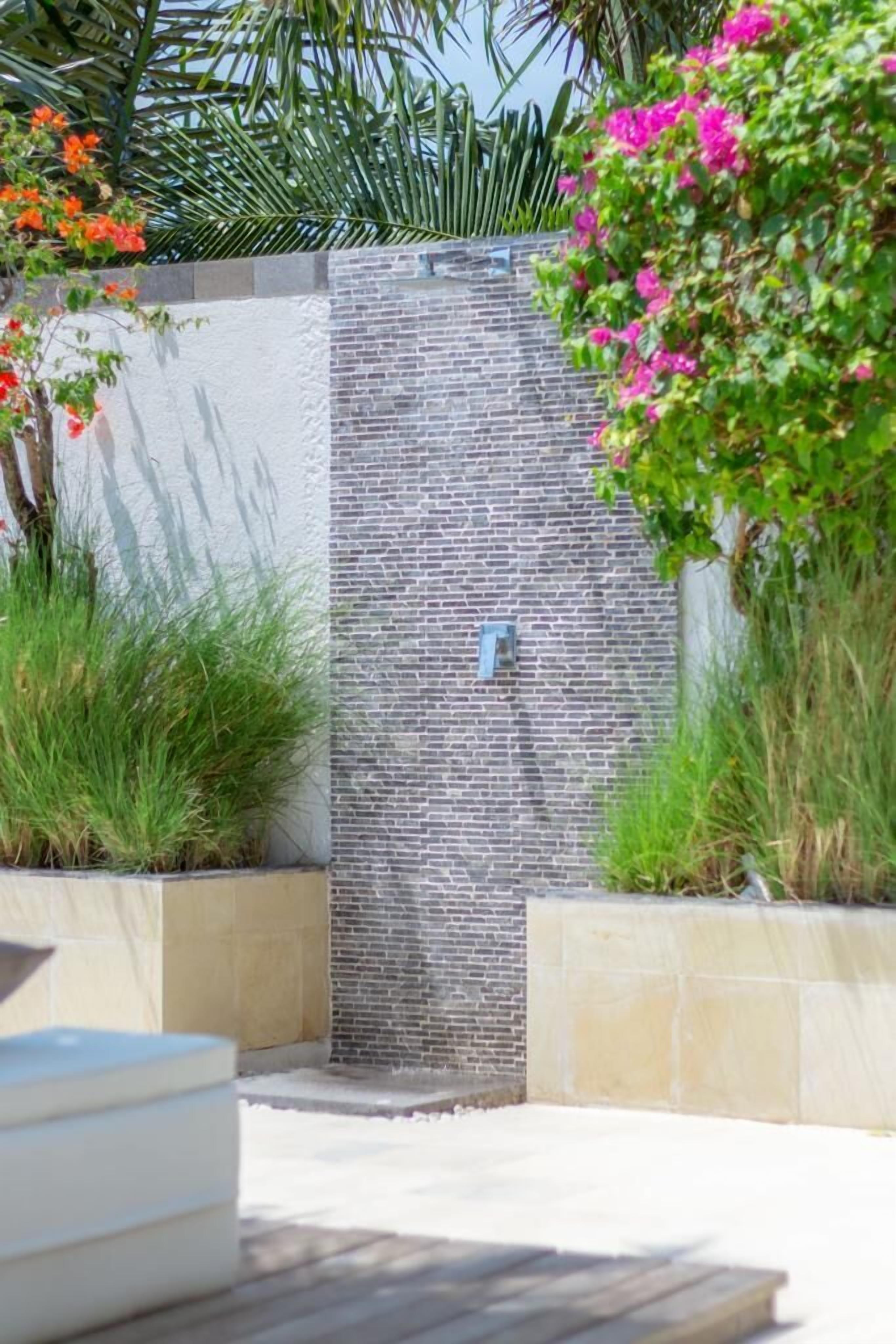 A modern outdoor shower area with a brick wall, surrounded by greenery and plants.