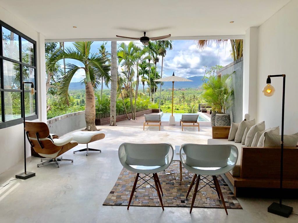 A spacious balcony with a view of lush greenery and mountains, furnished with modern chairs and a sofa.