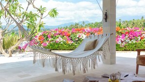 A hammock under a thatched roof, surrounded by wooden tables and vibrant flowers. - Lempuyang Boutique Hotel (Karangasem)