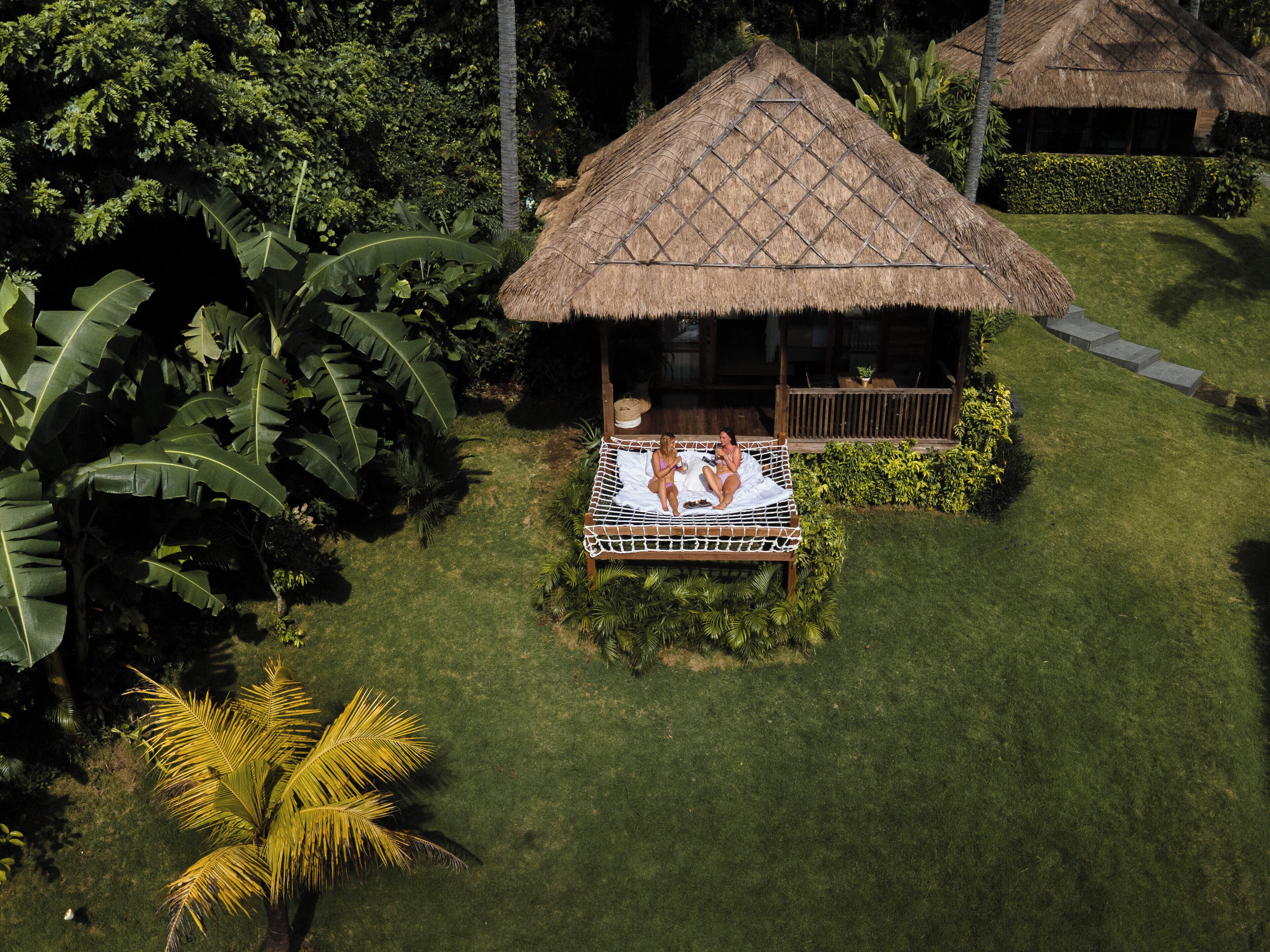 A thatched-roof hut with a hammock bed, surrounded by lush tropical vegetation.